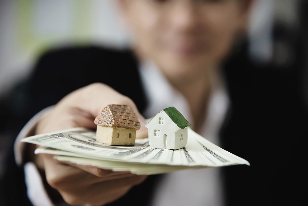 A person holding money with two miniature houses above it